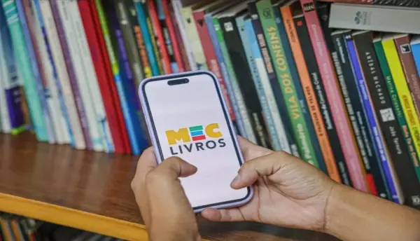 em uma biblioteca, pessoa utilizando um celular com a logo do mec livros em evidência